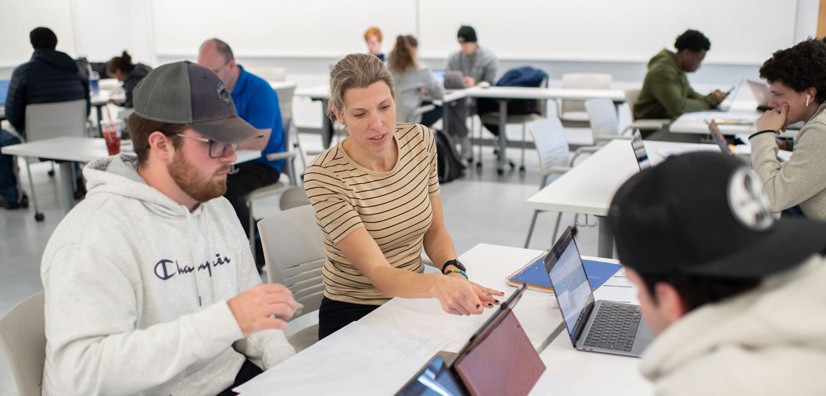 A student and an economics professor sit at a computer while discussing an assignment.