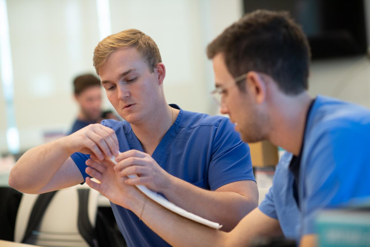 Two students in splinting lab exercise wearing blue scrubs.