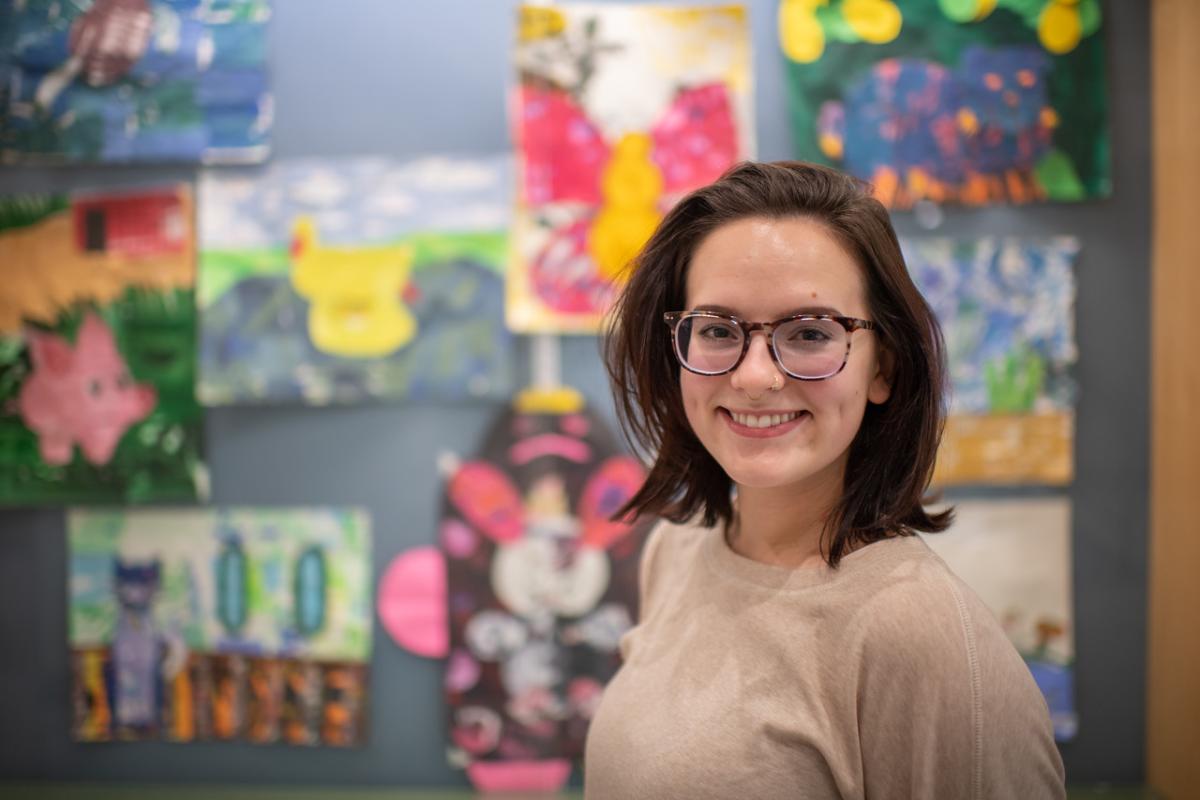 Visual Art licensure student smiling with student artwork behind her.