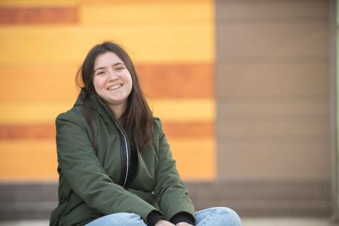 Westfield State student Cristina Ferraro sits in front of University Hall, a building with a wooden and metal facadeches and desserts in a restaurant decorated with an Alice in Wonderland theme.