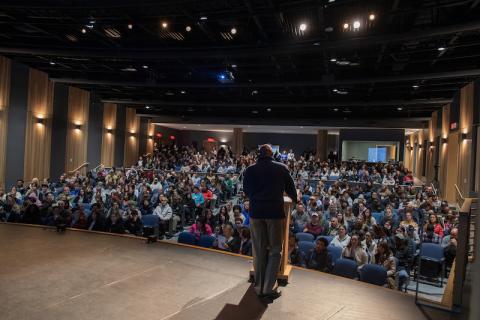 Accepted Student Day 2024. The photo shows Michael Mazeika, Director of Admission, speaking at a podium in the auditorium in Parenzo Hall. Hundreds of newly accepted students sit in the rows before him.