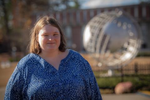 Melissa Costello, Class of 2022, posing in front of the campus globe. She's wearing a blue blouse and has the globe unfocused in the backround.