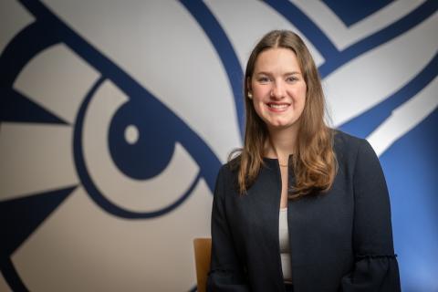 Elin-Maree Krupa, an international transfer student from Germany. She poses in front of a blue and white Owl mural and wears a dark blue coat jacket.