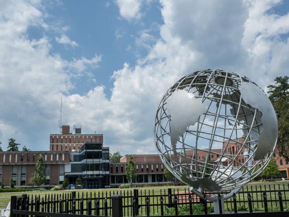 Globe on the campus green in the blue skies and white clouds with the Campus Center in the background