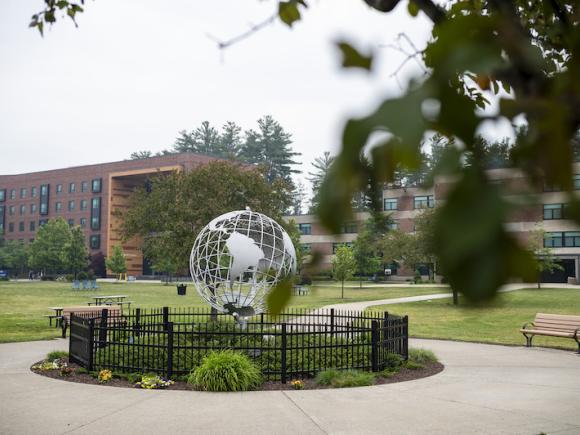 The campus globe sits under a cloudy, blue sky, with blurred foliage in the upper right-hand part of the screen.