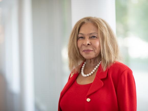 Dr. Linda Thompson in a red suit and standing in front of an open and bright mirror.