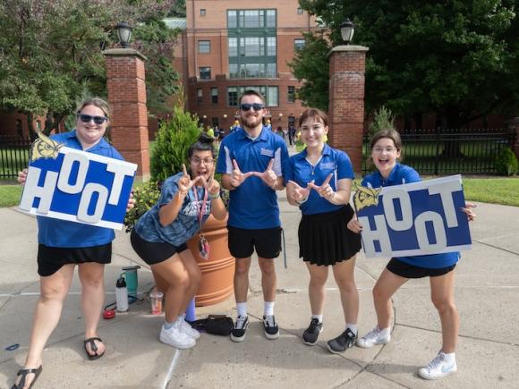 A small group of new students wearing blue shirts and holding blue and white signs that say, "Hoot Hoot". The new students are celebrating move-in weekend, which began on September 1.