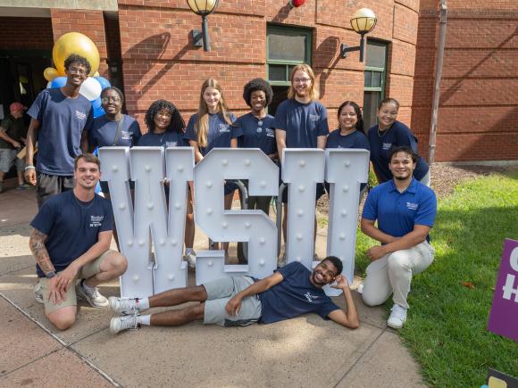 Residence Assistants smiling on the campus green with a WSU sign.