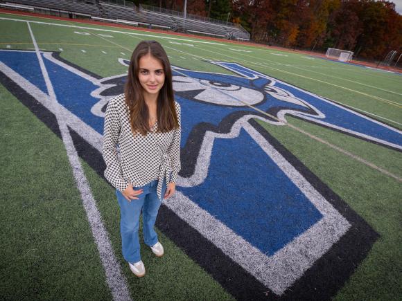 Student standing on campus football field smiling with WSU logo behind her.