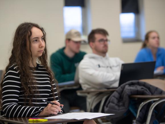 Students in a finance class sitting at desks listening to the instructor. 