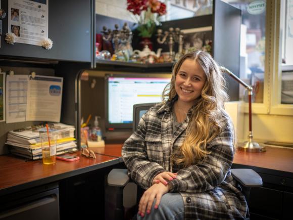 Career Services intern smiling at a desk with a computer screen visible in the background.