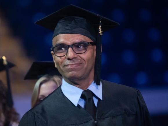 Graduate student wearing a cap and gown smiling during commencement ceremony.