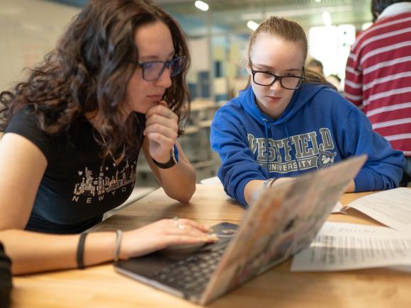 Two college students collaborating on an assignment using a laptop.