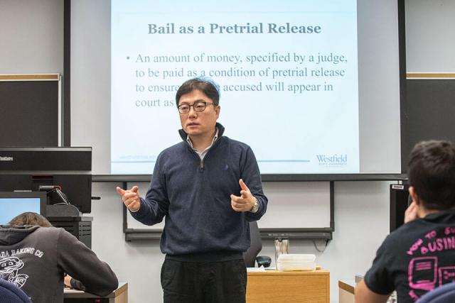 A professor instructs students from the front of a classroom.