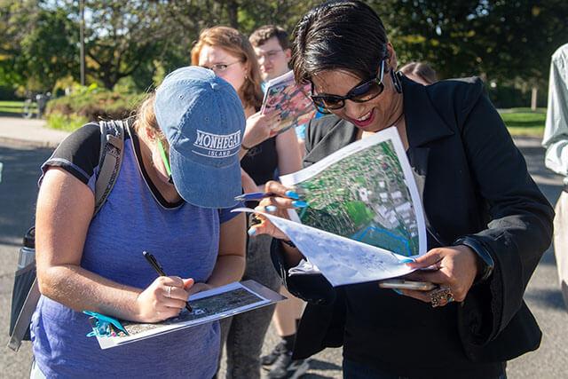 A group of students take notes and look at maps while outside.