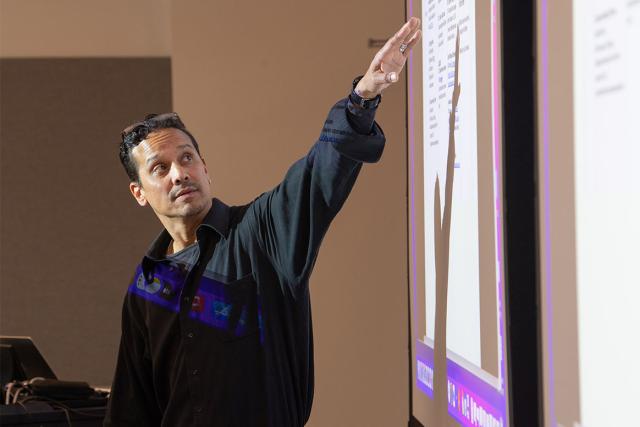 An education professor at Westfield State University motions to information projected on a screen while teaching.