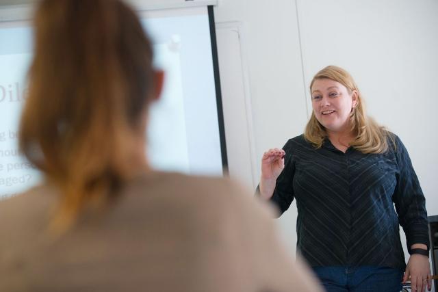 A Westfield State University professor instructs students while standing next to a projection screen.