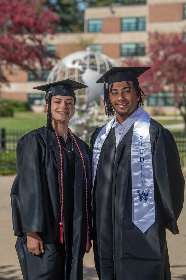 Two graduates smiling in front of the campus globe.