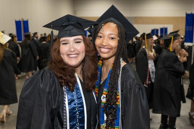 Two communication students wearing caps and gowns at commencement.