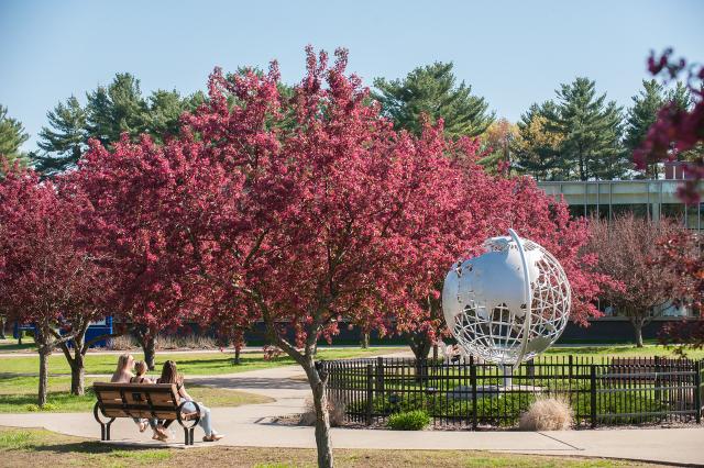 Campus globe in the spring with flowering trees behind it and three students sitting on a bench.