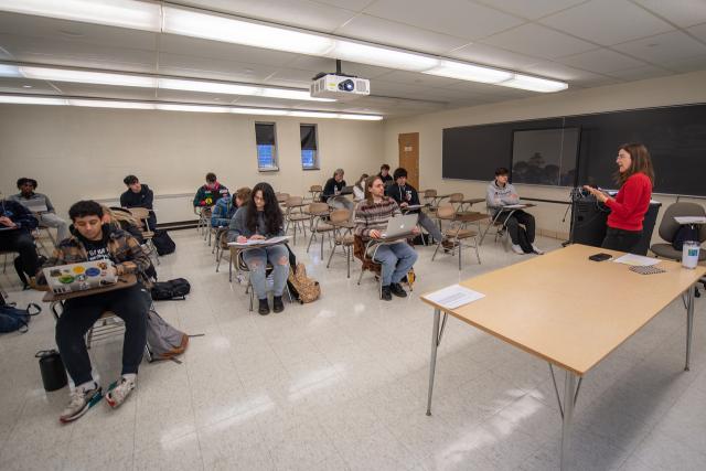 Classroom with students at desks and professor teaching in front of the classroom.