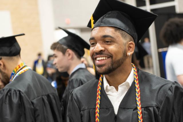 Student smiling wearing a cap and gown at commencement.