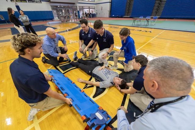 Faculty member demonstrating how to use a spine board to students in an athletic training class.
