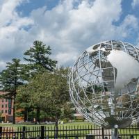 A photo of the campus globe during the summer season. The sky above is blue with clouds, and University Hall can be seen behind the globe itself.